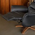 Fauteuil en cuir noir avec appui-tête et base bois pivotante, dans un intérieur chaleureux.