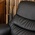 Fauteuil en cuir noir avec appui-tête et base bois pivotante, dans un intérieur chaleureux.