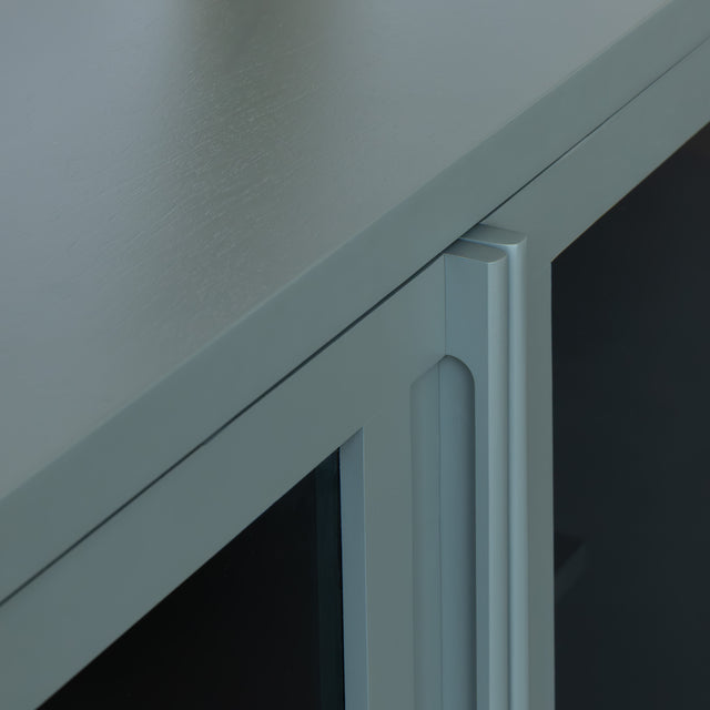 Buffet moderne vert sauge à portes vitrées fumées, décoré d’objets design dans un intérieur contemporain lumineux.
