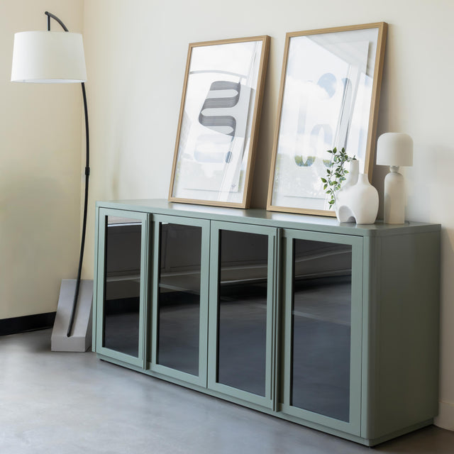 Buffet moderne vert sauge à portes vitrées fumées, décoré d’objets design dans un intérieur contemporain lumineux.
