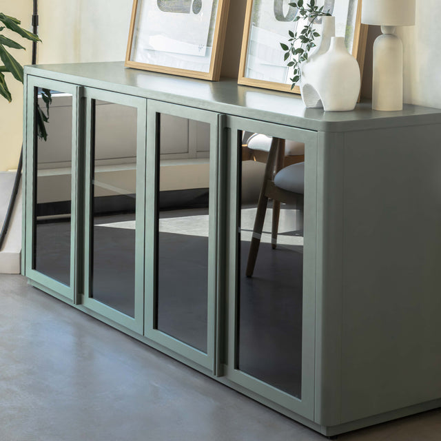 Buffet moderne vert sauge à portes vitrées fumées, décoré d’objets design dans un intérieur contemporain lumineux.