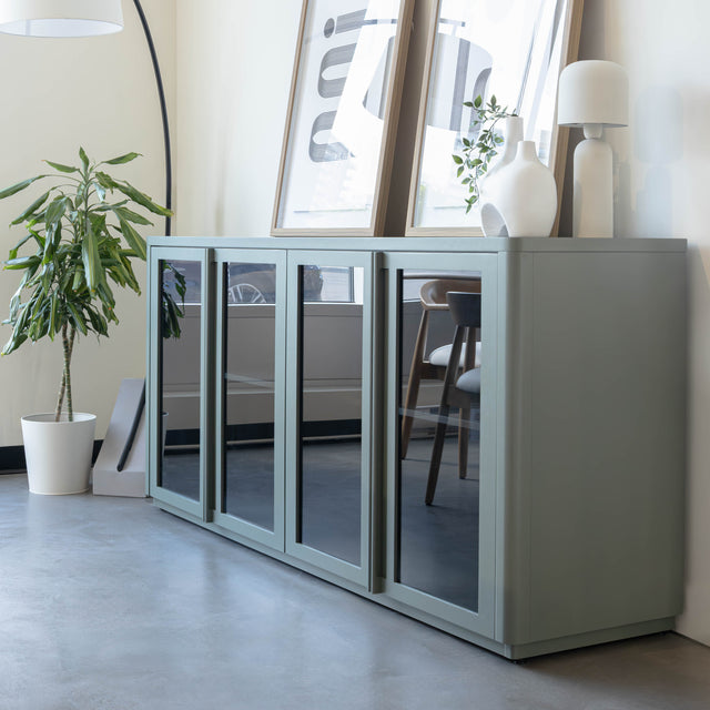 Buffet moderne vert sauge à portes vitrées fumées, décoré d’objets design dans un intérieur contemporain lumineux.