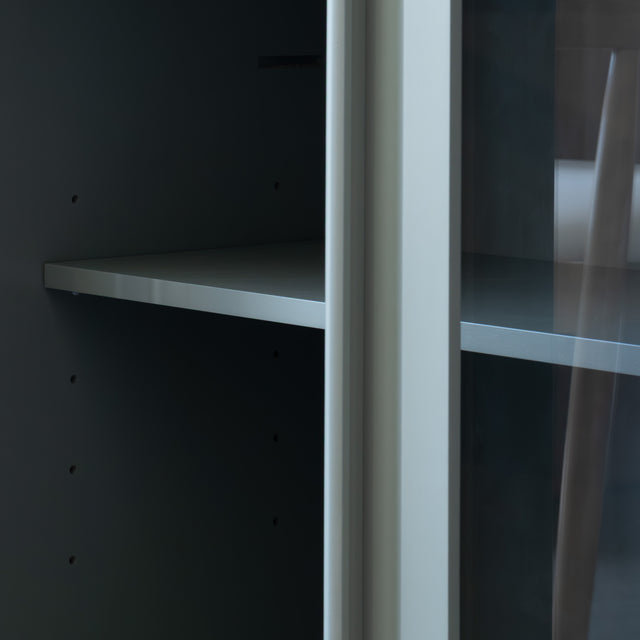 Buffet moderne vert sauge à portes vitrées fumées, décoré d’objets design dans un intérieur contemporain lumineux.