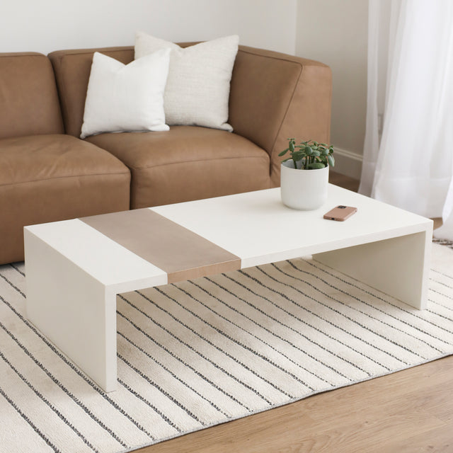 Table basse rectangulaire blanche avec insert en bois clair devant canape en cuir.