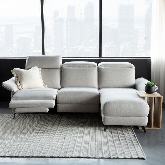 canape d angle gris clair avec tetiere et repose pieds reglables dans salon lumineux.
