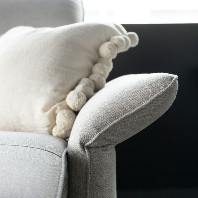 zoom sur accoudoir incline du canape gris clair avec coussin decoratif beige.
