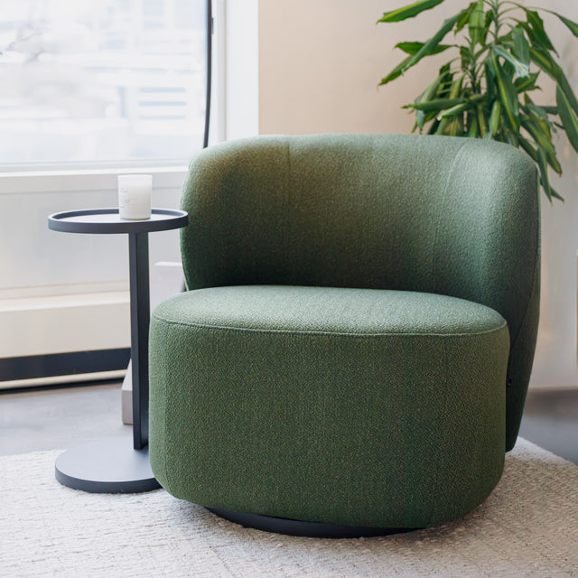 Fauteuil lounge vert en tissu bouclé avec base pivotante noire dans un salon moderne.