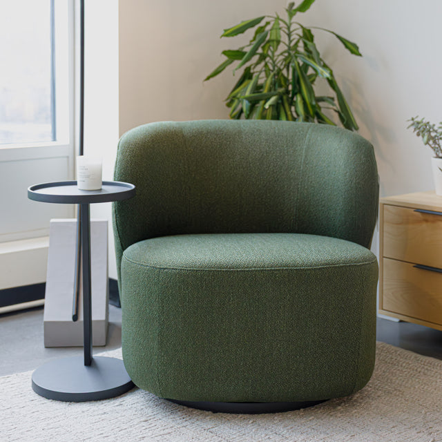 Fauteuil lounge vert en tissu bouclé avec base pivotante noire dans un salon moderne.