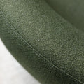 Fauteuil lounge vert en tissu bouclé avec base pivotante noire dans un salon moderne.