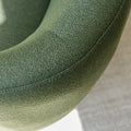 Fauteuil lounge vert en tissu bouclé avec base pivotante noire dans un salon moderne.