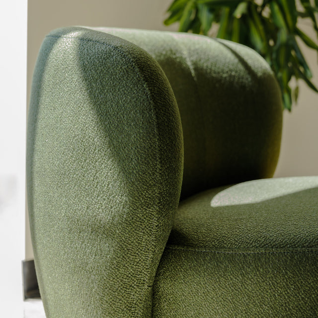Fauteuil lounge vert en tissu bouclé avec base pivotante noire dans un salon moderne.