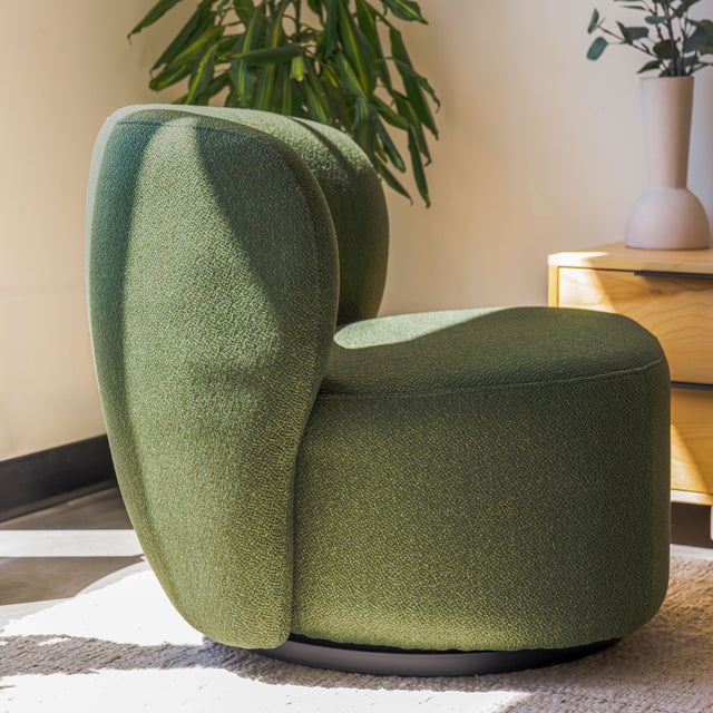 Fauteuil lounge vert en tissu bouclé avec base pivotante noire dans un salon moderne.