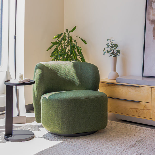 Fauteuil lounge vert en tissu bouclé avec base pivotante noire dans un salon moderne.
