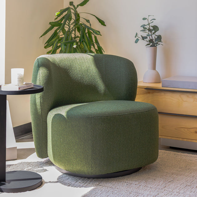 Fauteuil lounge vert en tissu bouclé avec base pivotante noire dans un salon moderne.