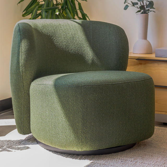 Fauteuil lounge vert en tissu bouclé avec base pivotante noire dans un salon moderne.