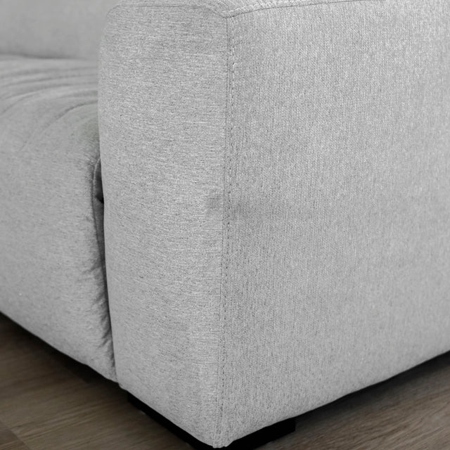 détail d’un accoudoir de canapé moderne en tissu gris clair, au tissage fin et à la texture légèrement chinée, posé sur un sol en bois clair.
