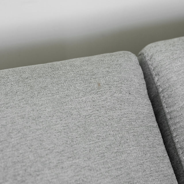 gros plan sur le tissu gris clair d’un canapé, montrant la texture douce et légèrement tissée de l’assise avec une petite marque discrète sur la surface.
