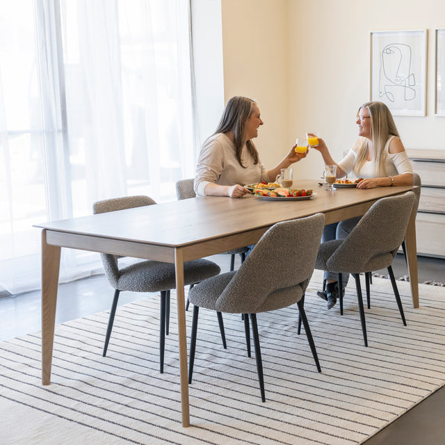 Table a manger en bois clair avec chaises grises sur tapis raye dans salle lumineuse.
