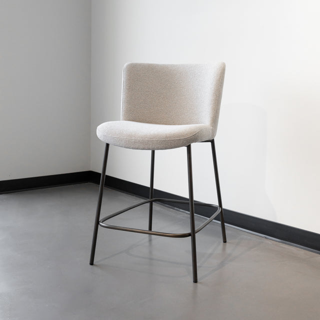 Tabouret de comptoir moderne en tissu beige avec piétement en métal noir, idéale pour cuisine ou îlot contemporain.