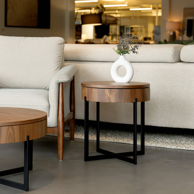 Table d’appoint ronde en bois noyer avec rangement, près d’un fauteuil beige.