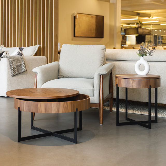 Table d’appoint ronde en bois noyer avec rangement, près d’un fauteuil beige.