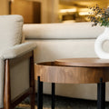 Table d’appoint ronde en bois noyer avec rangement, près d’un fauteuil beige.