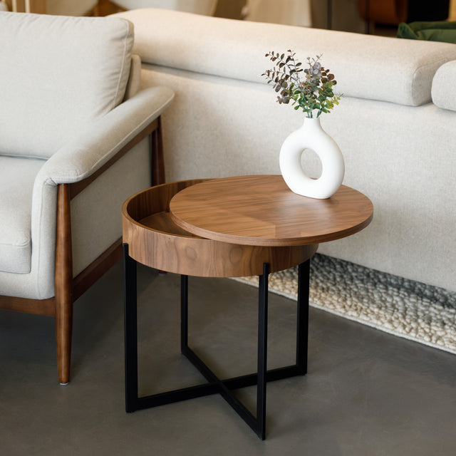 Table d’appoint ronde en bois noyer avec rangement, près d’un fauteuil beige.