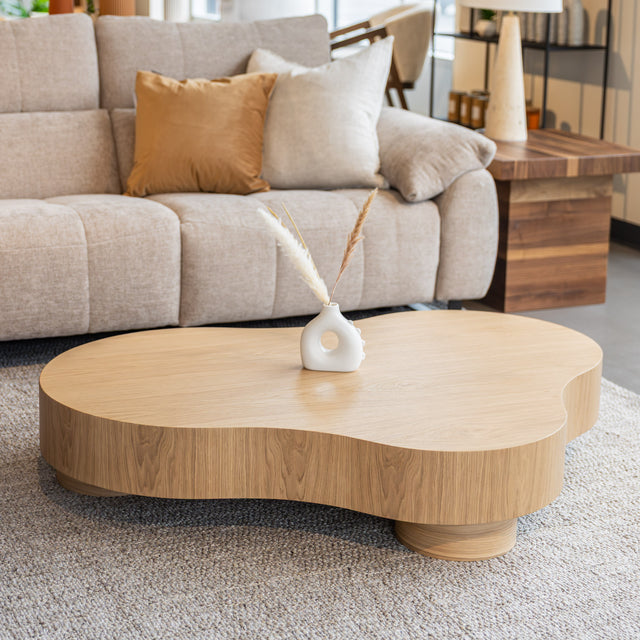 Table basse organique en bois clair dans un salon moderne avec un sectionnel gris.