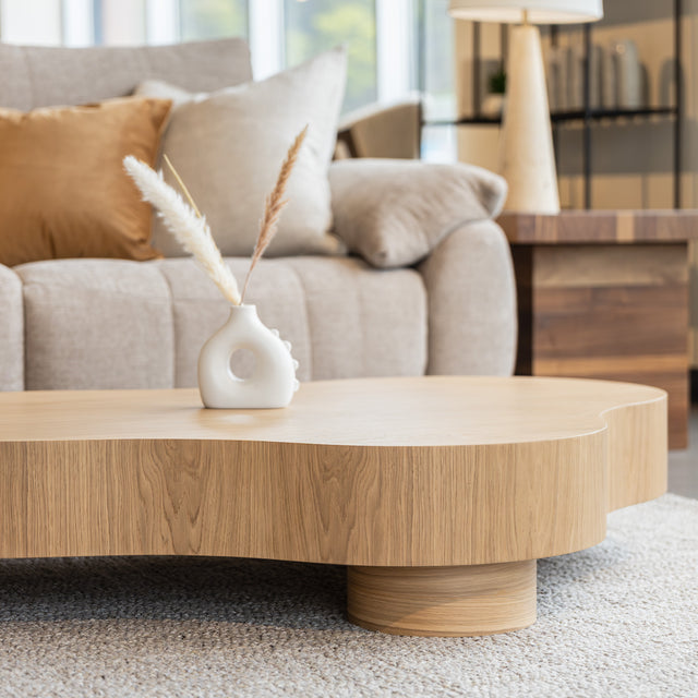 Table basse organique en bois clair dans un salon moderne avec un sectionnel gris.