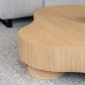 Table basse organique en bois clair dans un salon moderne avec un sectionnel gris.