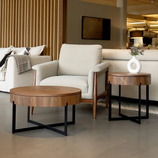 Table basse ronde en bois noyer avec rangement, près d’un fauteuil beige.