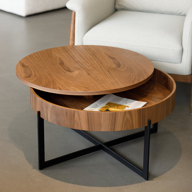 Table basse ronde en bois noyer avec rangement, près d’un fauteuil beige.