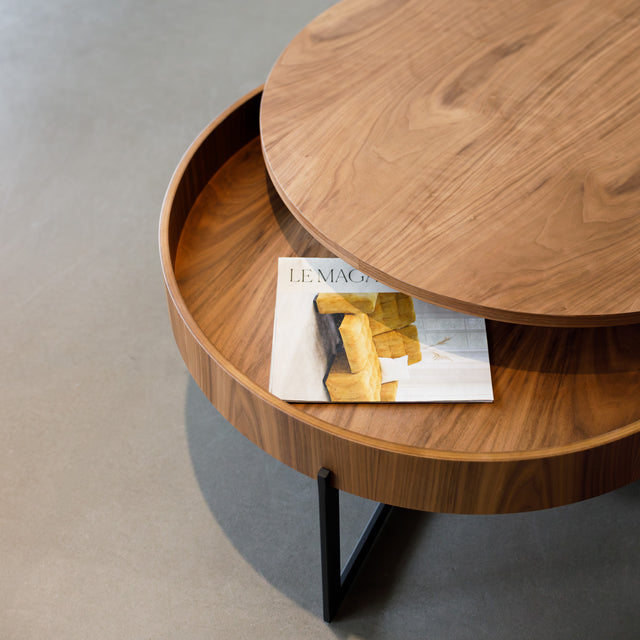 Table basse ronde en bois noyer avec rangement, près d’un fauteuil beige.