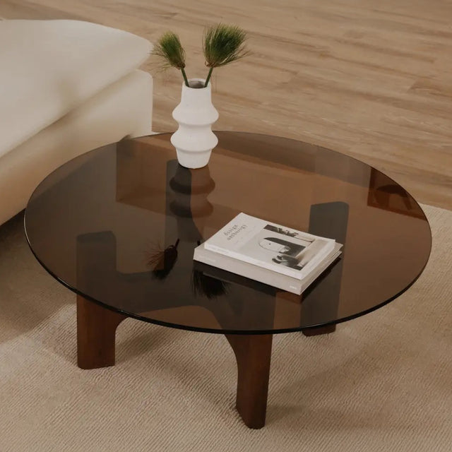 Table basse ronde avec plateau en verre teinte brun et base en bois courbe.