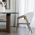 Table ronde en bois avec chaises beige et vase blanc dans deco lumineuse et epuree.
