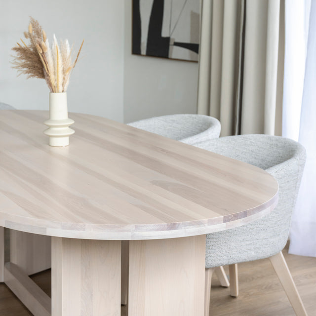 Table ovale en bois clair avec chaises crème modernes dans salle a manger lumineuse.
