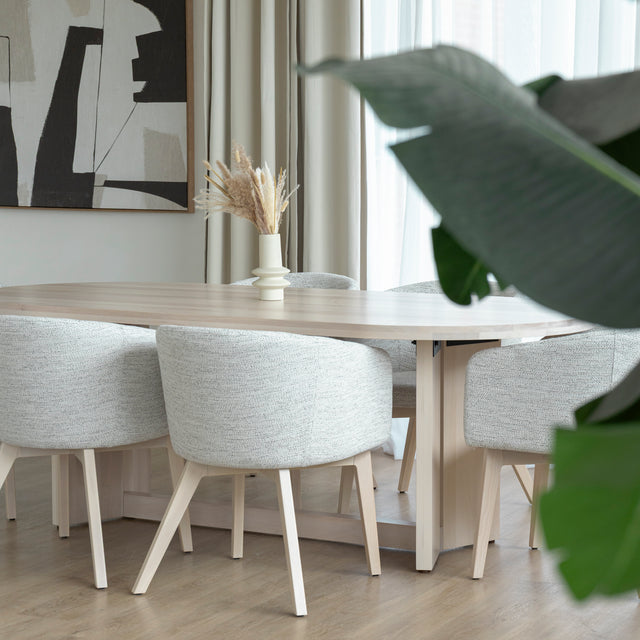 Table ovale en bois clair avec chaises crème modernes dans salle a manger lumineuse.