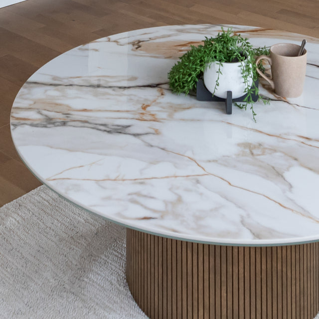 Table basse ronde en porcelaine imitation marbre avec pied en bois strie dans un salon moderne beige.