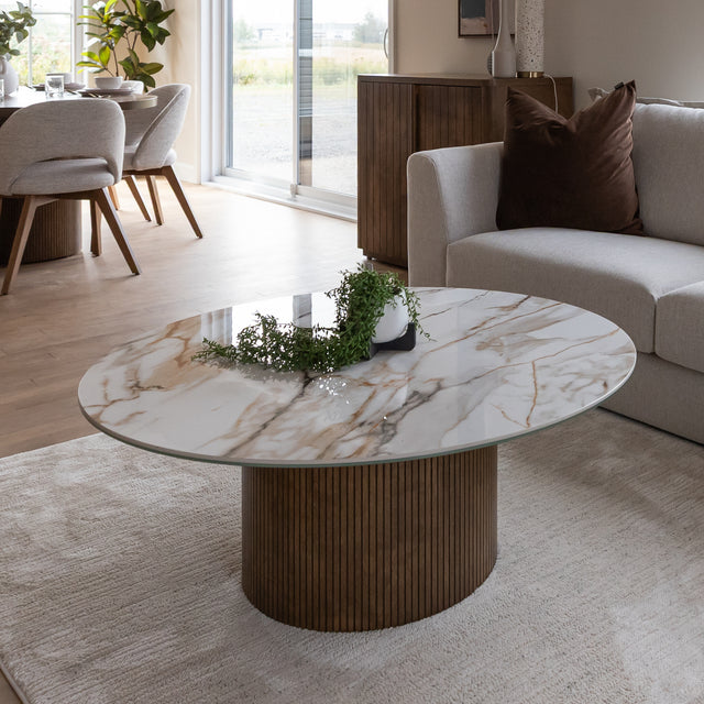 Table basse ronde en porcelaine imitation marbre avec pied en bois strie dans un salon moderne beige.