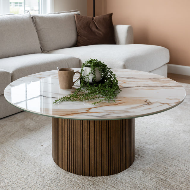 Table basse ronde en porcelaine imitation marbre avec pied en bois strie dans un salon moderne beige.