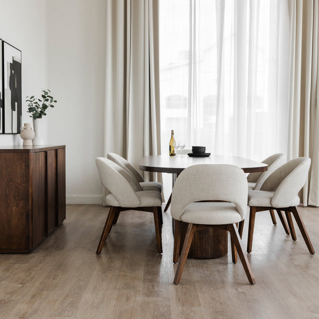 Salle a manger moderne avec table ovale en bois fonce et chaises beige sur plancher clair.
