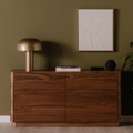 Commode en bois noyer au design contemporain avec lampe dorée et décoration minimaliste sur mur vert olive.