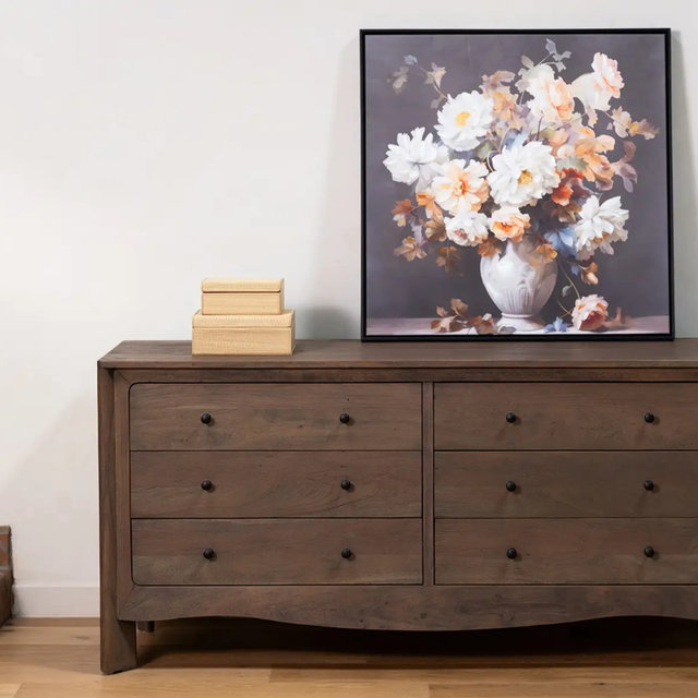 Commode en bois avec six tiroirs et tableau floral décoratif posé dessus, style chaleureux et élégant.