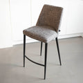 Tabouret de bar design avec assise en tissu brun/gris et pieds en metal noir, ideal pour cuisine moderne.