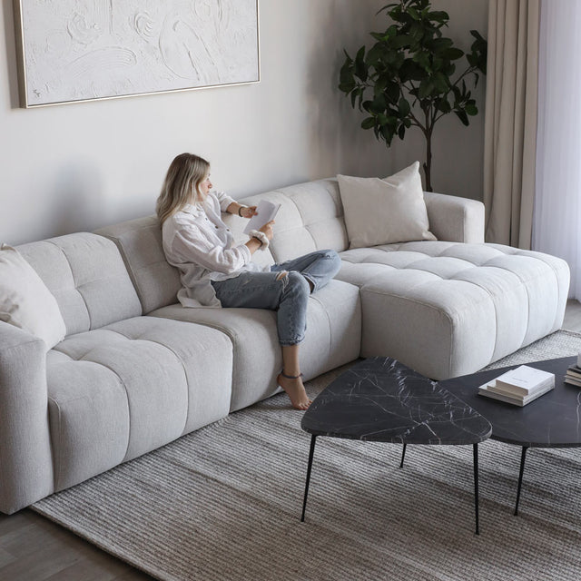 Salon moderne avec canape d angle beige clair matelasse et table basse noire en marbre.